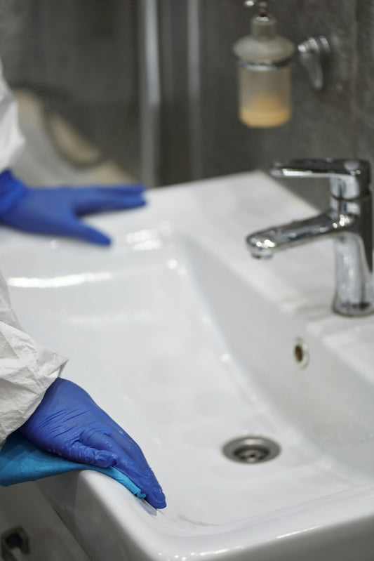 Persoon die badkamer schoonmaakt met doekje en reinigingsmiddel voor een frisse en hygiënische ruimte